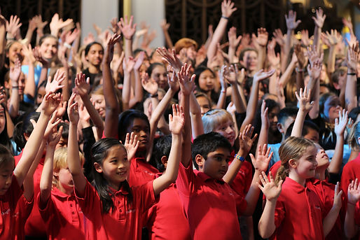 Singers of all ages performing, with hands raised