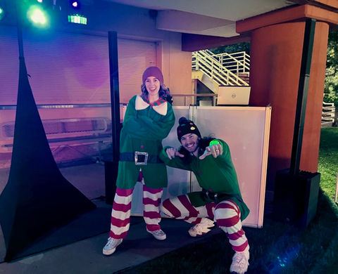 Man and woman dressed as elves in front of DJ booth.