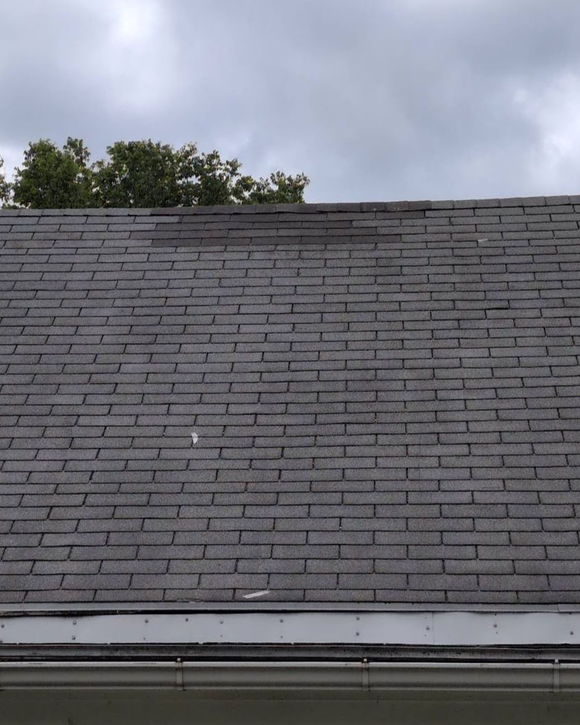 Gray asphalt shingle roof with damaged and lifted shingles along the ridge