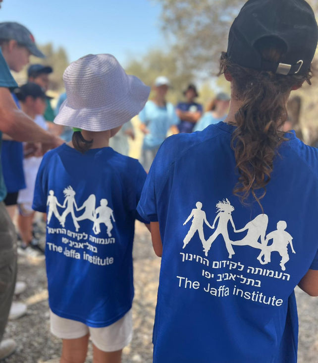 Two girls in Jaffa Institute T-shirts facing a circle during an activity with hats and pony tails