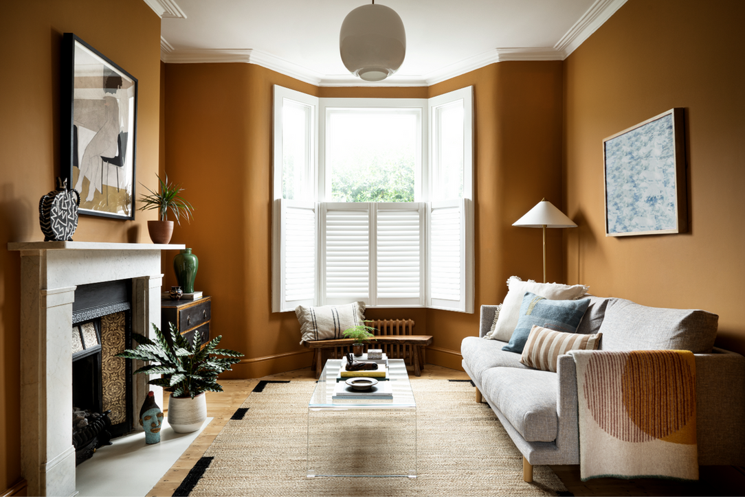 Large living room with large bay window, walls are painted in a deep yellow ochre tones with white ceiling 