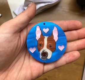 A photo of a hand holding an ornament with a dog's face on it, made out of acrylic
