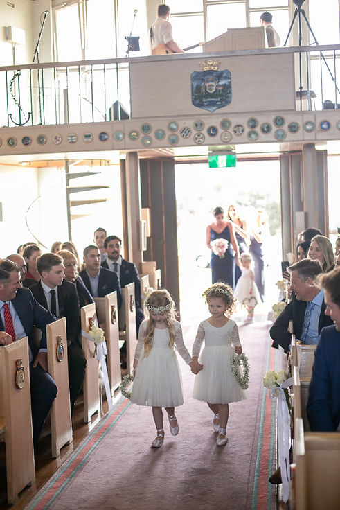 Flower girls walking down the aisle at the wedding ceremony at HMAS Watson Chapel. Wedding photography by best Sydney wedding photographer, Grant Hoskinson Photography.