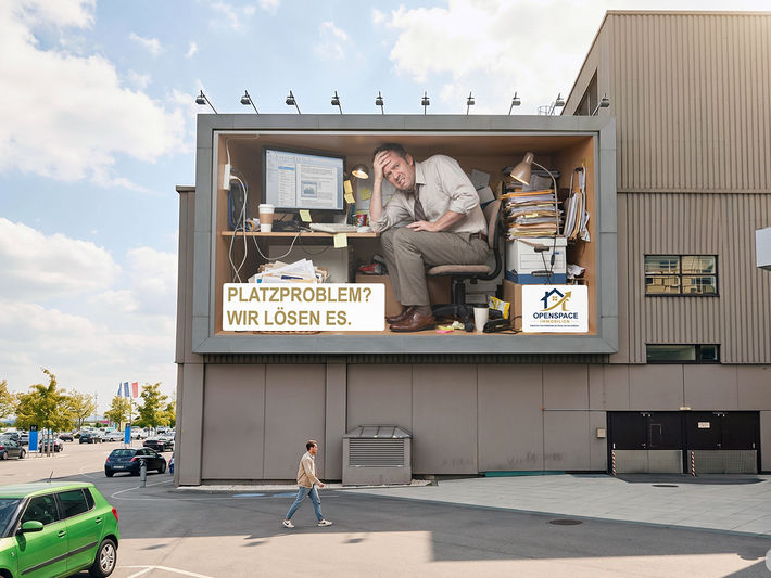 High-impact anamorphic 3D billboard mockup by Brandspace3D on a commercial building facade, showcasing a CGI advertisement for Openspace Immobilien with a cramped man in a small office box to promote experiential Out-of-Home (OOH) advertising.