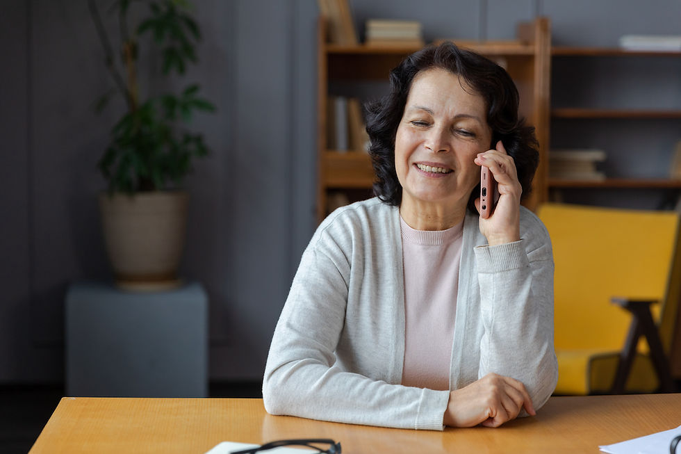 A woman with dark hair wearing a light gray sweater smiles as she talks on the phone about her favorite things.
