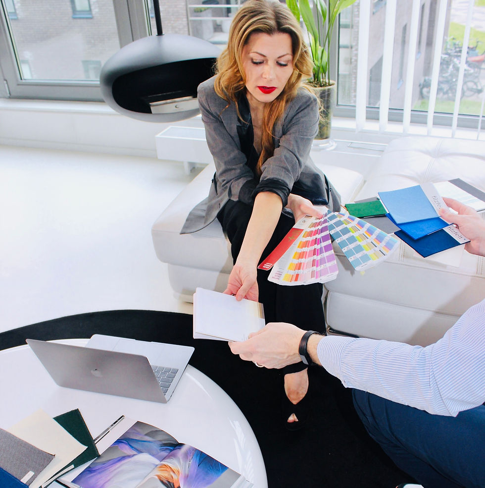 Christa Binder speaking with a customer during a design consultation, both smiling and engaged in conversation. The setting features a warm, well-lit interior with curated decor elements in the background