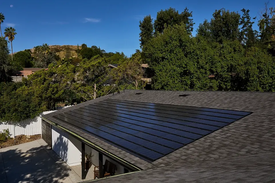 Un techo con tejas solares, vegetación al fondo.