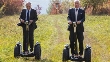 two men in suits on segways in a meadow