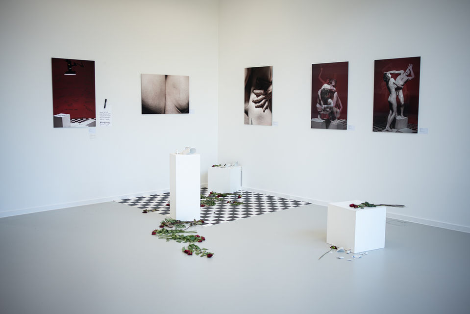 Wide view of a spacious gallery room with photographs hanging on the walls and minimalistic installations on the floor.