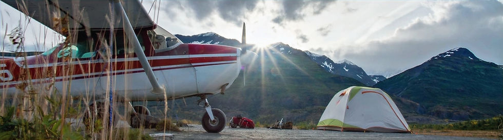 Bush plane parked by a campsite at sunset in the mountains