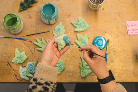 Hands painting ceramic leaves during a community arts workshop in London