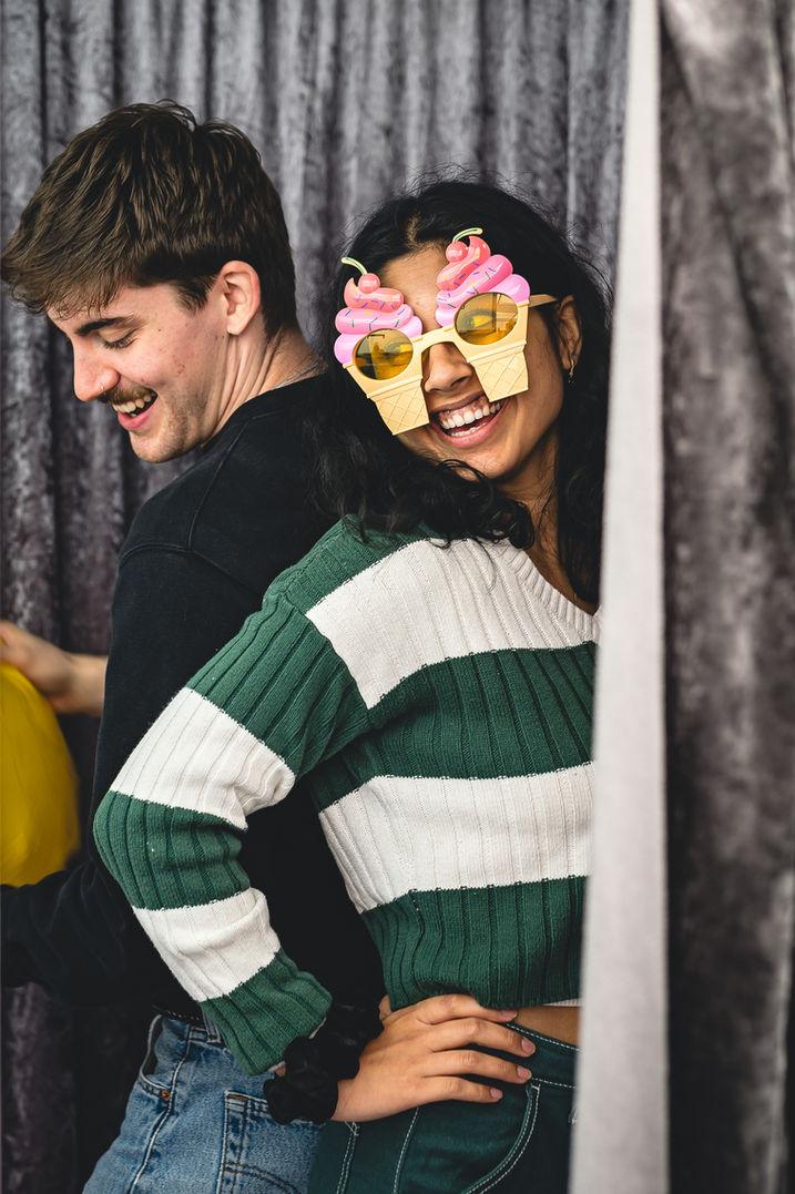 Two students having fun in a Photo Booth dressing up during welcome week, image captured by university photographer Aaron Scott Richards