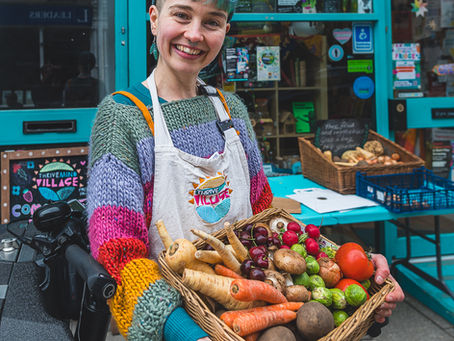 Volunteer holding a basket of rescued vegetables outside Thrive Mind Village community fridge in Derby