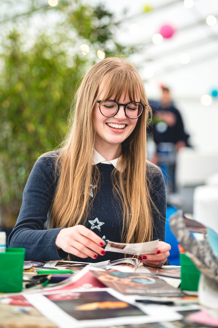 A student wearing glasses smiles as she takes part in some art activities, image captured by university photographer Aaron Scott Richards