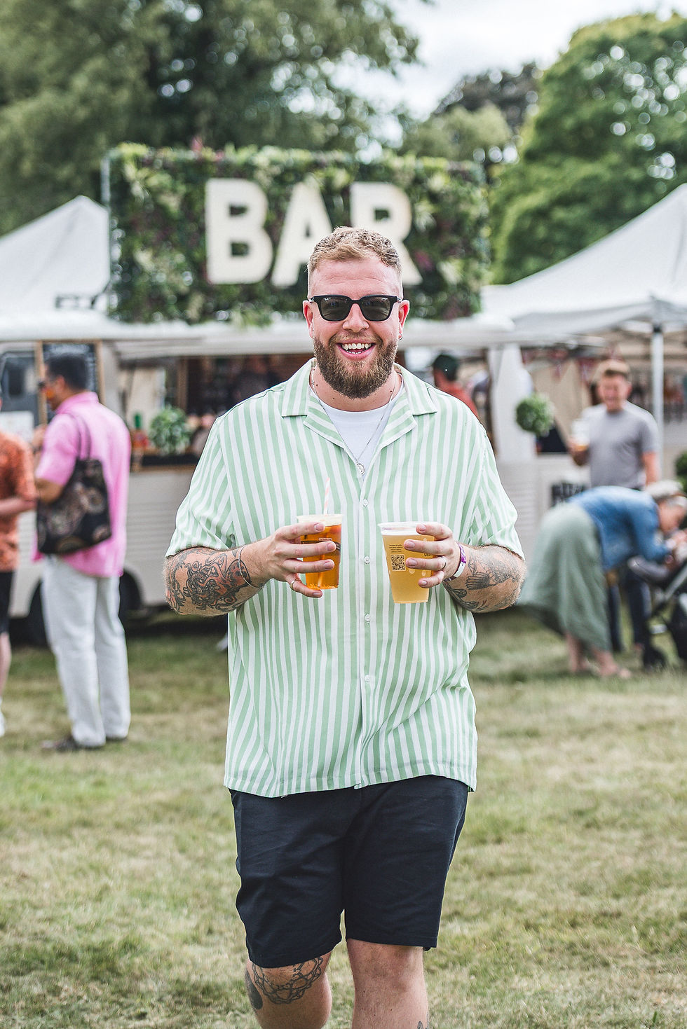 Smiling festival visitor holding two drinks in front of the Vanderbar mobile bar
