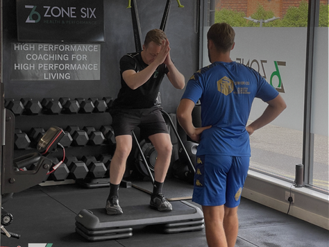 Physiotherapist supervising a man performing step-ups on a platform in a Zone Six gym.