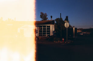 Small coffee shop with “Coffee” sign and wood siding, captured at sunset with long shadows and empty parking lot. Left half of the shot is burnt by light exposure on the film roll.