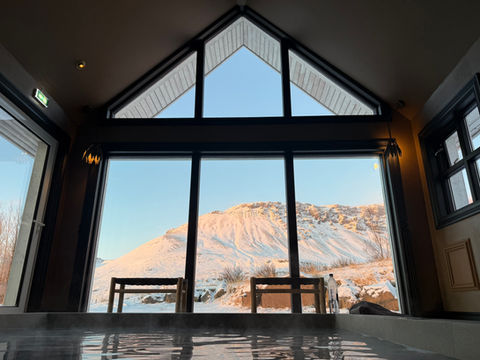 Indoor hot tub area with large triangular windows framing sunlit snow-capped mountains and clear blue sky.
