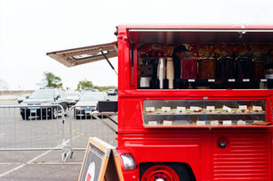Bright red coffee truck parked in a lot, side window open showing drinks and pastries for sale.