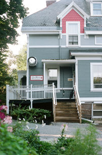 Light blue Victorian house exterior with white trim, front steps, and guest entrance sign visible beside railing.