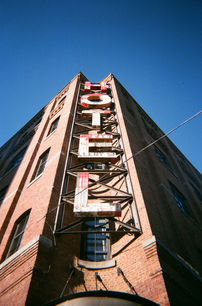 Low-angle view of vintage brick hotel facade with red neon ‘HOTEL’ sign against clear blue sky.