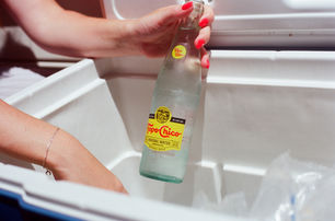 Close-up of hand pulling a Topo Chico mineral water bottle from a white cooler filled with ice.
