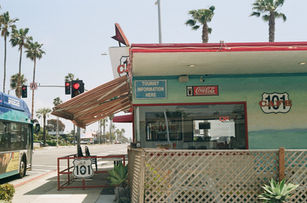 Roadside restaurant with a Coca Cola sign and cream lattice fence surrounded by palm trees and blue sky.
