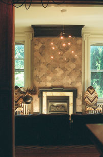 Living room scene with geometric tiled fireplace, contemporary chandelier, patterned chairs, and large windows.