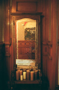 Tall vintage mirror framed in carved wood, reflecting hallway artwork, with cluster of pillar candles at base.