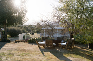 Outdoor seating area with wooden chairs and a fire pit, surrounded by trees and desert landscape in late afternoon light.