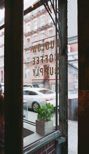 White Ludlow Coffee Supply logo on glass café door, reflected view of street and building outside.