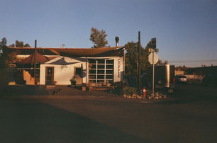 Small coffee shop with “Coffee” sign and wood siding, captured at sunset with long shadows and empty parking lot.