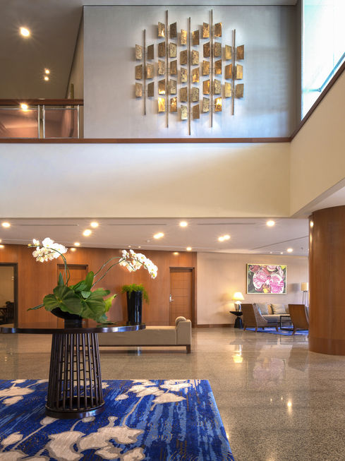 Spacious hotel lobby atrium featuring polished floors, a brass wall sculpture, a central floral display, and a comfortable seating area.