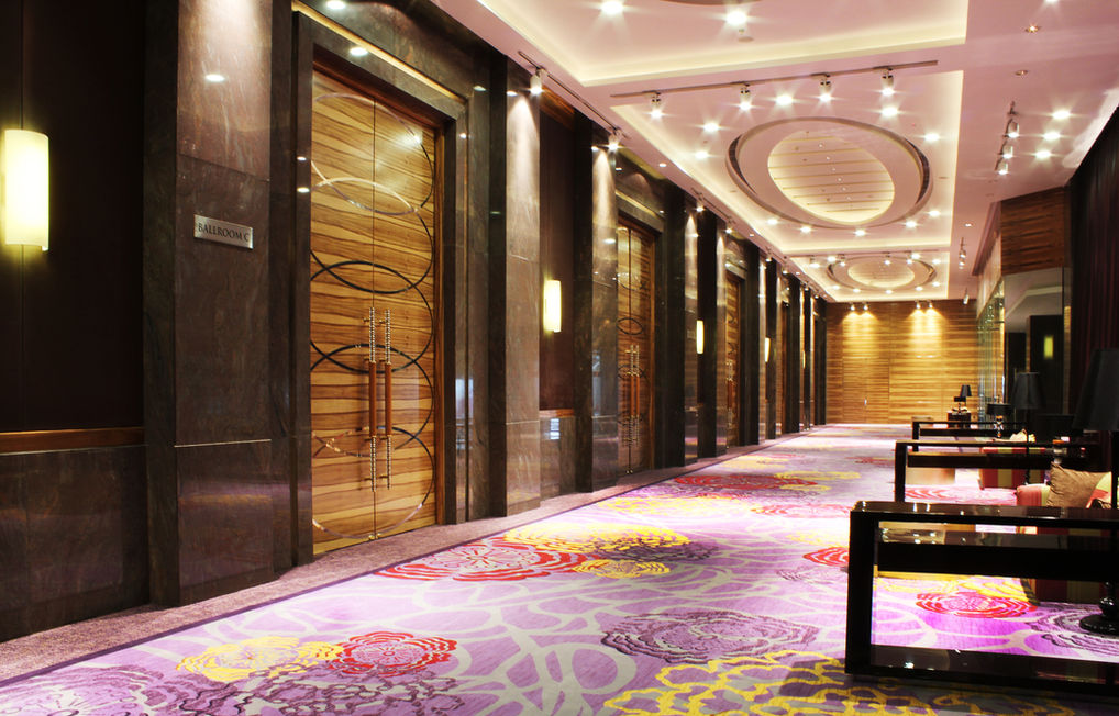 Angled view of a ballroom entrance featuring decorative wood double doors labeled Ballroom C, dark marble columns, and patterned purple floral carpeting.
