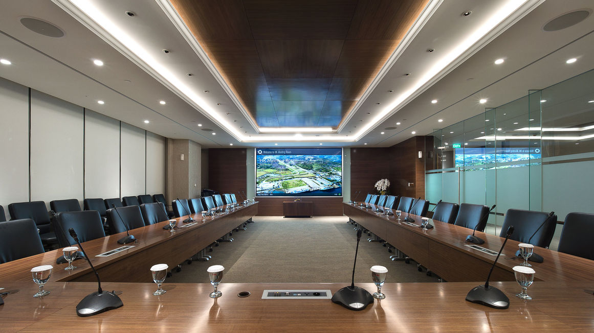 Large executive boardroom featuring a U-shaped conference table with microphones, comfortable black leather chairs, and a front presentation screen.