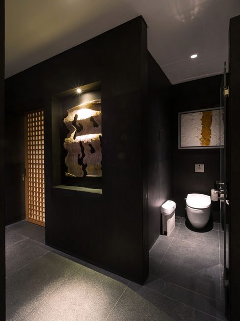 Modern dark-toned restroom featuring a toilet, an illuminated decorative wall niche, and a wooden lattice door.