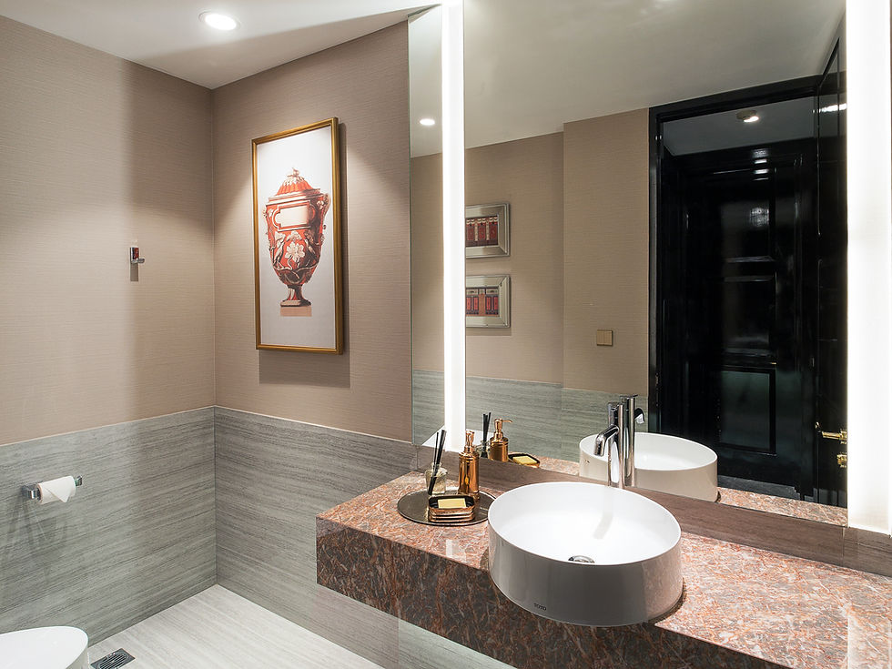 Kamar mandi modern dengan wastafel putih, meja marmer, cermin besar, dan lukisan vas merah di dinding beige.