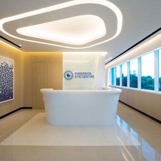 A clean, modern medical reception lobby featuring a white curved front desk, wood-paneled walls, large windows with outdoor views, and a glowing corporate logo.