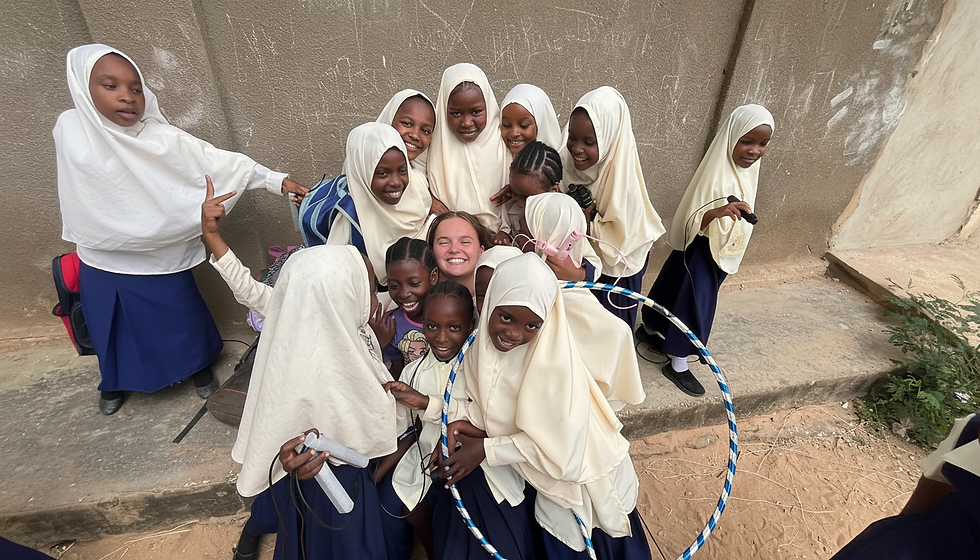 Landscape photo of a smiling volunteer surrounded by local school children in uniforms, warm colors, wide landscape format.