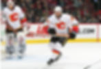 A hockey player in Calgary Flames gear skates energetically on the ice, showcasing a classic wooden stick during a competitive match.