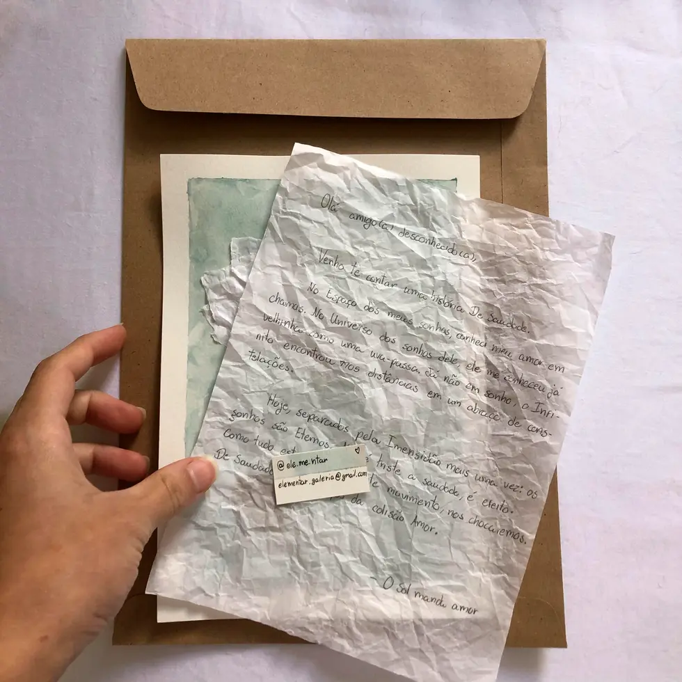 Envelope pardo com folha de papel de seda branca amassada, trazendo carta manuscrita a um destinatário desconhecido e pequeno cartão artesanal com formas de contato.