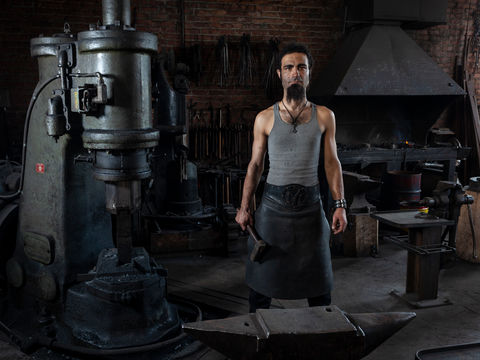 Forgeron dans son atelier avec un décor industriel et un éclairage avec un flash, ambiance obscure