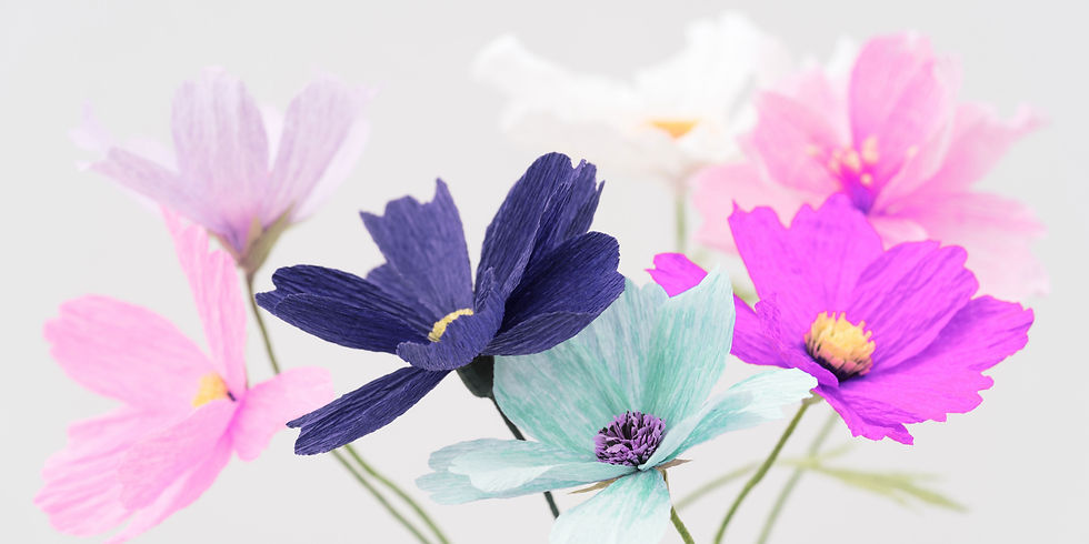 Colorful paper flowers in pink, purple, blue, and white on a soft white background, creating a delicate spring mood.