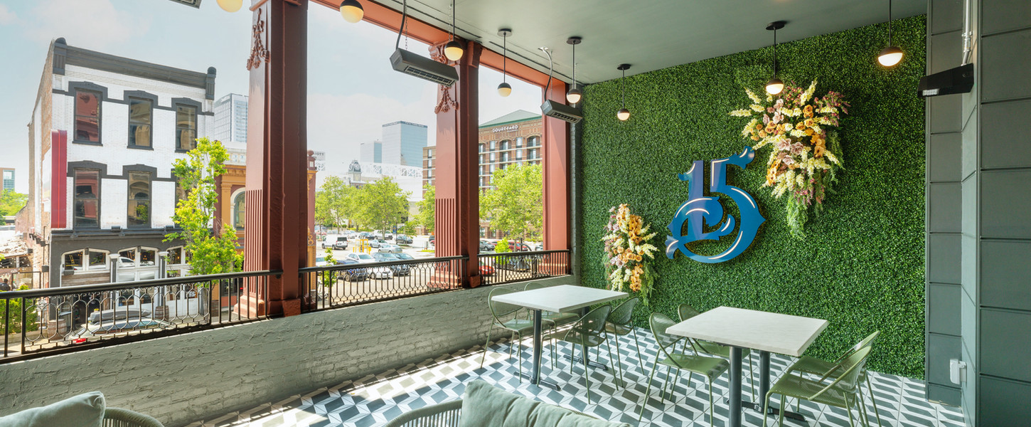 A photo of the interior of number 15 louisville showing green chairs, and a green plant wall with a large, blue number 15 on it.