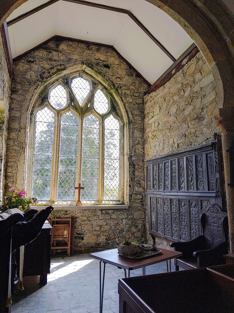 Stone-walled chapel room with large stained glass window, wooden chairs, a floral bouquet, and a table with a cross, creating a serene atmosphere.
