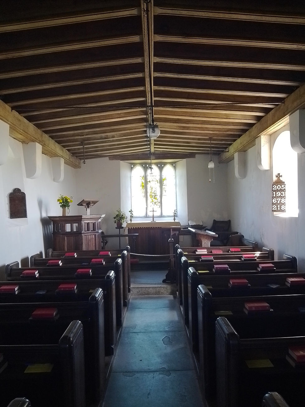 A church interior with wooden pews and hymn books. Sunlit altar at front, stained glass window, hymn numbers on wall, peaceful ambiance.