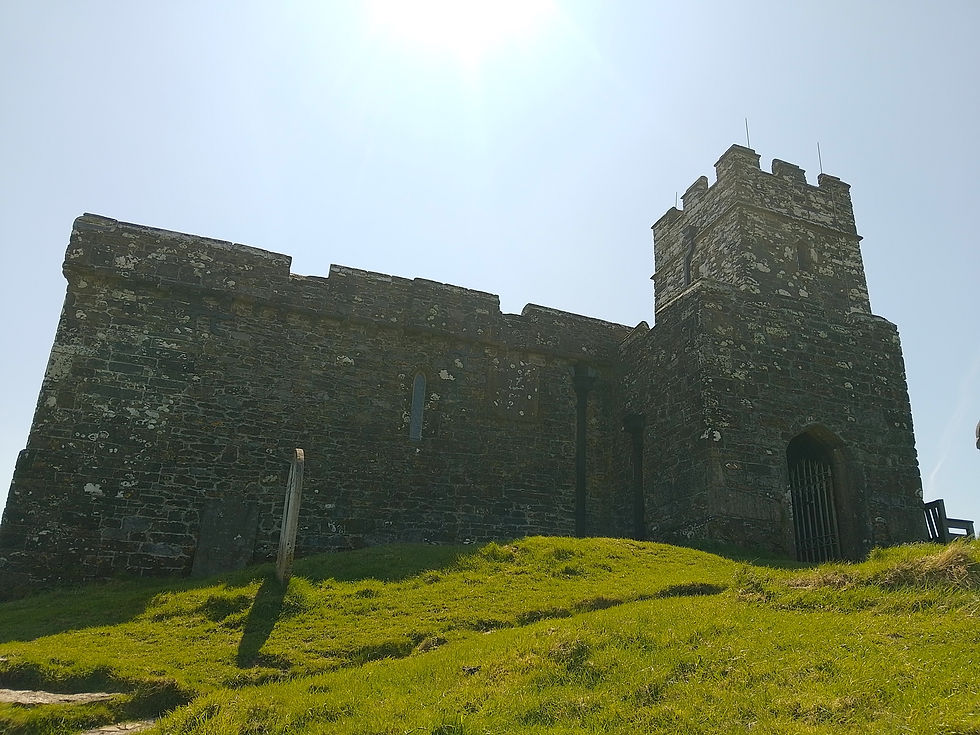 Old stone castle on a grassy hill under a bright blue sky. Sunlight casts shadows, creating a serene and historic atmosphere.