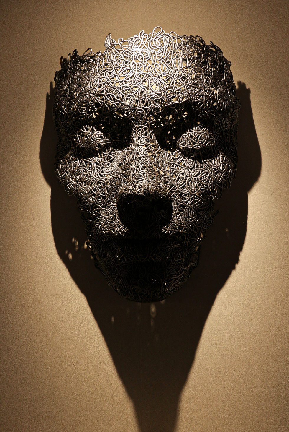 Dark sculpted face emerging from wall – contemporary art with tribal intensity