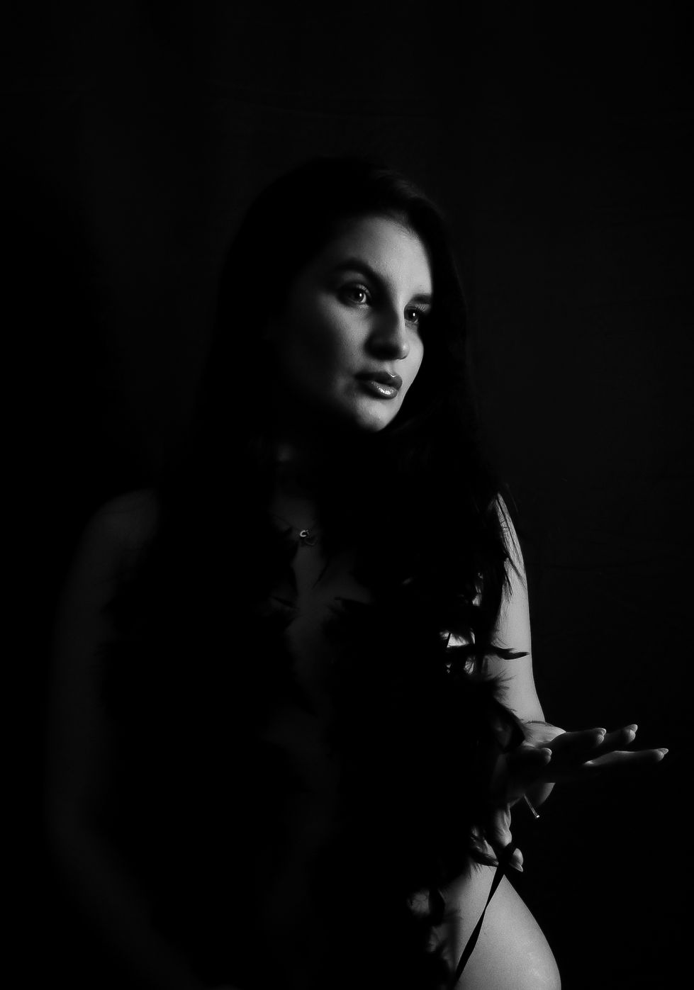 Woman in darkness holding a rose branch, with a calm yet intense expression, partially lit from the front.