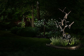 a flying birds statue art sits in the middle of a dark garden